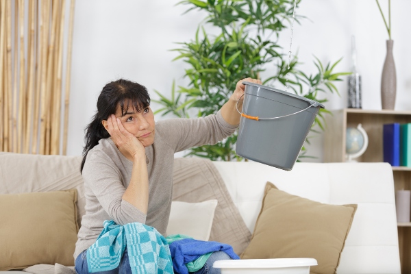 A homeowner holds up a bucket to catch water dripping from a leaking roof.