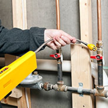 Person using a yellow device to test gas pipes in a wall installation.