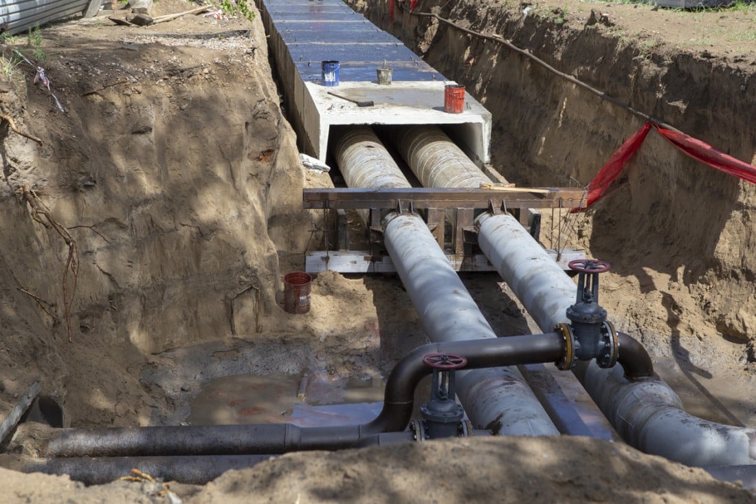 Underground pipes installed in a trench with visible valves and construction materials.