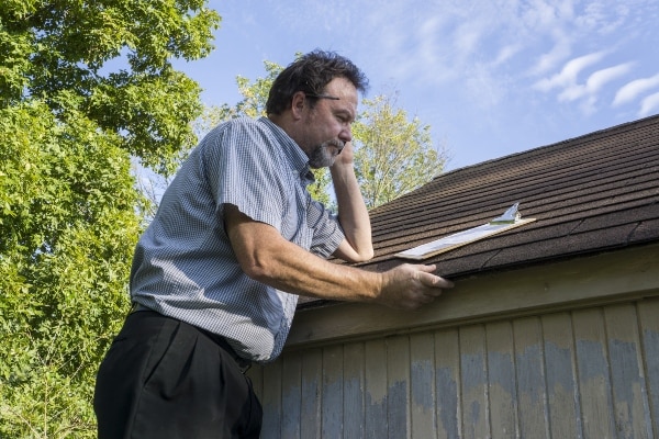 Man inspecting roof with clipboard outdoors under blue sky.